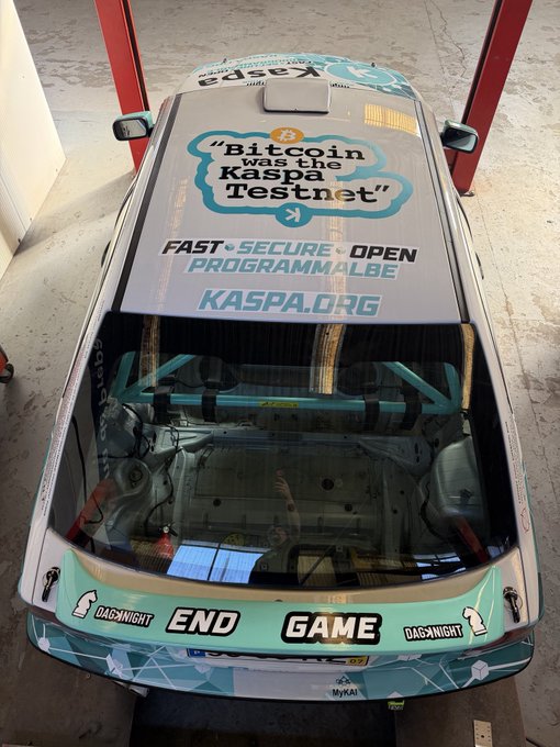 A race car with a teal and white livery features roof text reading '"Bitcoin was on Kaspa Testnet"' along with 'FAST · SECURE · OPEN PROGRAMMALBE KASPA.ORG', and a rear banner displaying 'END GAME' with 'DACA-NIGHT' logos.