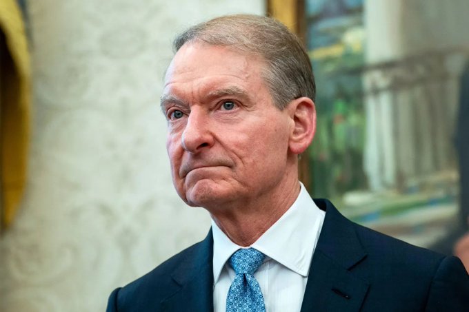 An older man in a dark suit and blue tie looks off to the side with a serious expression in an ornate room. The image likely depicts a financial regulator or government official, relevant to the post about new SEC rules affecting cryptocurrencies like $ETH, $SOL, and $BNB.