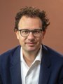 A photo of a man with glasses and brown hair in a dark suit, likely Dario Amodei, CEO of Anthropic, which the accompanying post compares in valuation and revenue to Walmart to question whether AI valuations constitute a bubble.