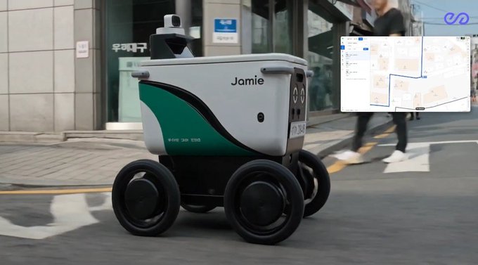 iced coffee machine with a green and white design, labeled "JAMIE" and "ROCKY-ROAST", moves on wheels along a city street lined with buildings and trees.