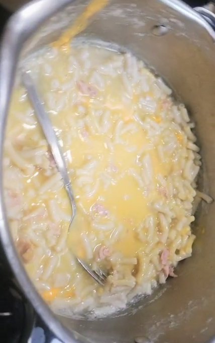 A metal pot filled with orzo pasta in a creamy cheese sauce mixed with bits of ham, with a fork resting inside.