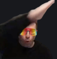 A blurry video still of a man with dark hair wearing reflective orange sunglasses, his hand raised above his head against a black background.