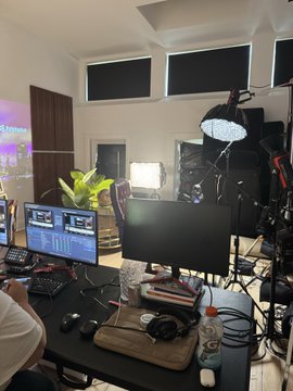 A behind-the-scenes view of a podcast or streaming studio setup, featuring laptops with editing software, professional lighting equipment, microphones, and a water bottle on the desk, while a person works at the setup—matching the post's description of visiting @MarketBubble's studio to congratulate them on reaching 1M followers and witness @Jackkk's clipping process.