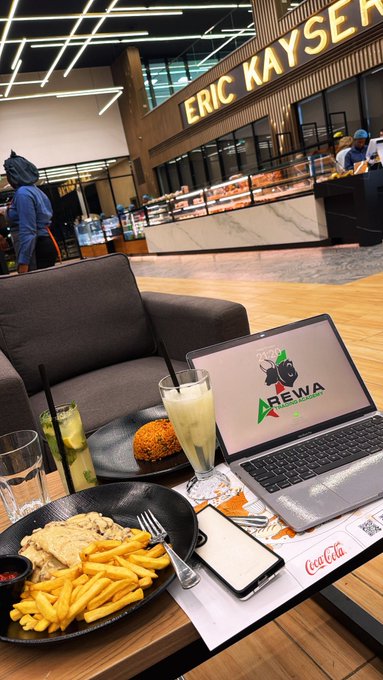 A meal of fries, rice, fried chicken, and drinks is enjoyed at "ERIC KAYSER" café, with a laptop displaying an "AREWA" sticker on the table. The scene captures a well-deserved treat, matching the post's message of celebrating a $500 profit withdrawal by indulging in a relaxing dine-out experience.