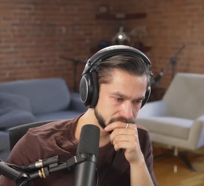 The image features a man wearing headphones, sitting in front of a microphone while looking down at his hand. The background includes a couch and a chair, suggesting that he might be in a living room or a similar indoor setting. The caption reads "Tom Lee is down eight billion dollars on $ETH and Vitalik decides to write a sci fi novel". This post seems to be related to the man's situation with Tom Lee, as they both have something to do with money and investments.