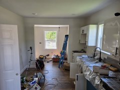 A kitchen interior is under renovation, with plastic sheeting covering cabinets, tools scattered around, and an open door leading to another room.
