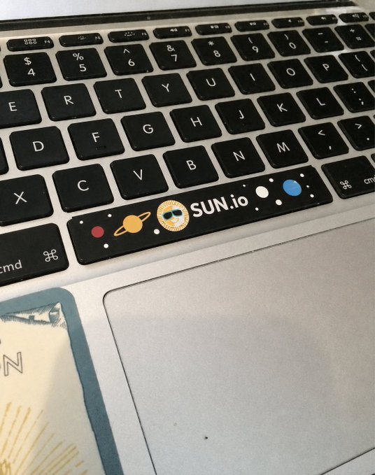 A close-up of a MacBook keyboard space bar featuring a decorative sticker with planets and the text 'SUN.io'.
