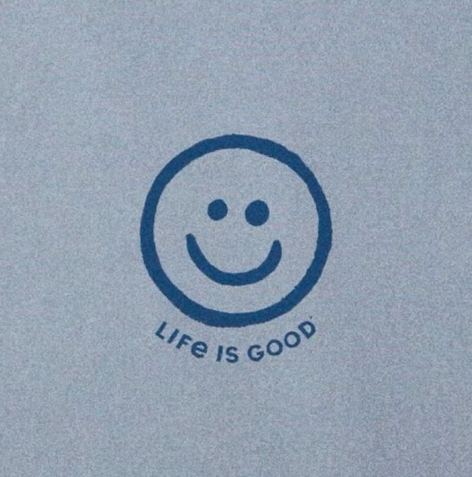 A simple blue smiley face logo with the text 'LIFE IS GOOD' printed underneath on a light blue/grey fabric background.
