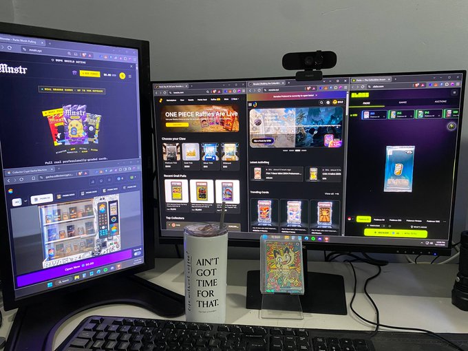 A dual-monitor computer setup displays trading card websites including 'ONE PIECE Battles Are Live!' and a digital trading card on a stand, with a tumbler reading 'AIN'T GOT TIME FOR THAT' in the foreground.