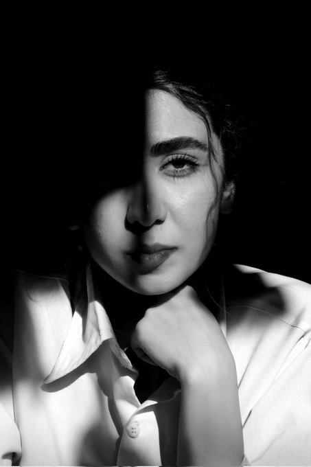 The image features a woman with long dark hair, wearing a white shirt, and her face is partially obscured by a shadow cast from above. The background appears to be black, which contrasts with the woman's white shirt and highlights her presence. The photo has been edited or altered in some way, possibly for artistic purposes or to create a specific mood. The image does not contain any text, but it seems to be related to the post about the moon.