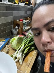 A person in a kitchen eating a carrot, with lettuce and green onions visible on a cutting board in the background.