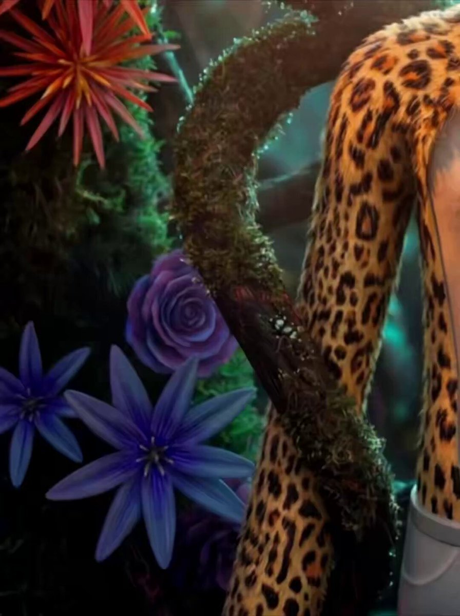 The image features a close-up of a leopard's leg with its tail wrapped around a tree branch adorned with purple flowers. The background includes more trees and flowers, creating an overall natural setting for the scene. In the corner of the image, there is a caption that reads "Some people contribute to the @BoredApeYC in one lane. @apewhale contributes in many. Whether it'S building tools, supporting community initiatives, helping new members find their footing, or creating products that celebrate Ape culture, he's constantly showing up and making the".