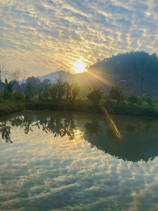 A serene sunset over a pond with mountains in the background, the golden light reflecting beautifully off the water's surface.