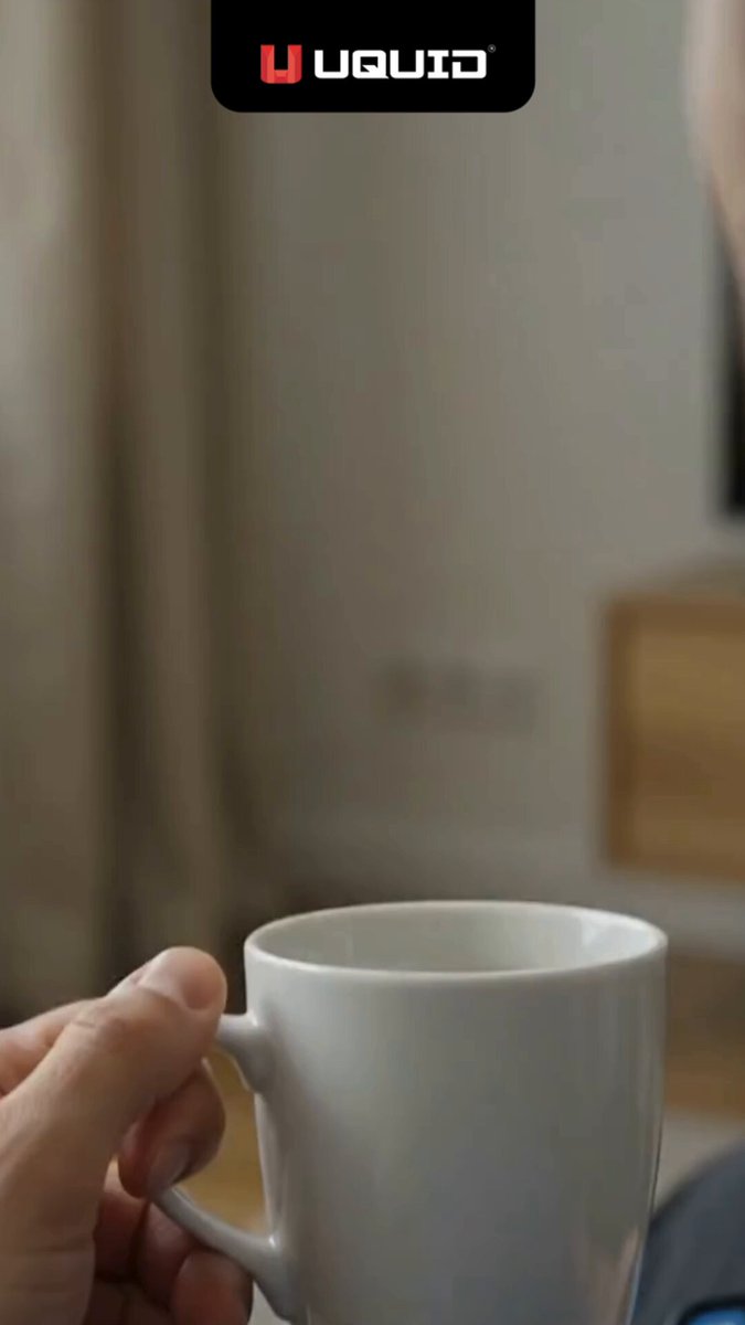 The image shows a person holding a white cup filled with coffee or tea, possibly enjoying their beverage while browsing for event tickets. The background of the photo features a window, suggesting that they are sitting indoors. The text "How easy can it be to get tickets with USDT on UQUID Tickets? You tell us!" is present in the image, which seems to be related to the post about purchasing tickets online.