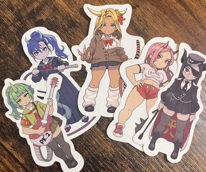 Five anime-style character stickers with horns, tails, and weapons are arranged on a wooden surface, matching the post about NFTs that have come to life and are running around energetically in a manga world, including visible labels "あにゃ組" and "PK-2".