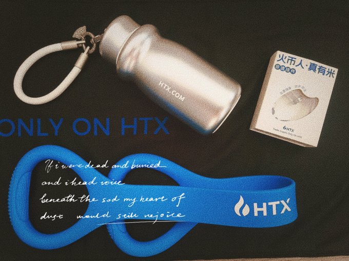 A silver HTX-branded water bottle, a small NFT-style card reading "火币人·真有米" with the HTX logo, and a blue wristband displaying the poetic inscription "It were dead and buried and i head voice beneath the sod my heart of dust would seek rejoice" alongside the HTX flame logo are arranged on a black "ONLY ON HTX" mat—promotional merchandise celebrating Huobi's 13th anniversary and its resilient global journey.
