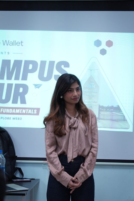 A young woman with long dark hair, wearing a pink blouse with a bow tie, stands in front of a presentation screen displaying "CAMPUS TOUR," "Wallet," and "FUNDAMENTALS / WEB3," likely as one of the speakers featured in the post about an insightful Blockchain, Web3, and Cake Wallet session.