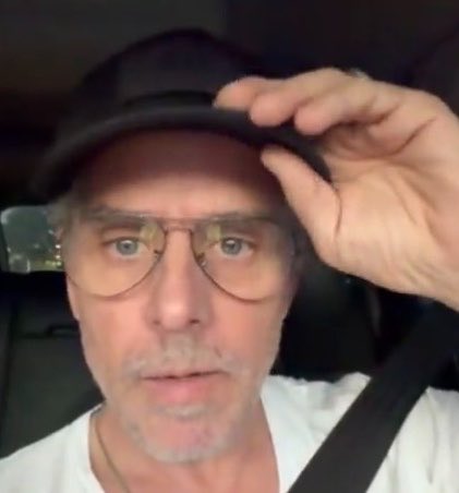 The image shows a selfie of a man with gray stubble, wearing aviator glasses and a black cap, adjusting the brim with his hand while seated inside a vehicle. The accompanying post references Hunter Biden and Elon Musk regarding a $LAPTOP memecoin account, with the man's appearance in the selfie appearing to depict Hunter Biden in a casual, candid moment.