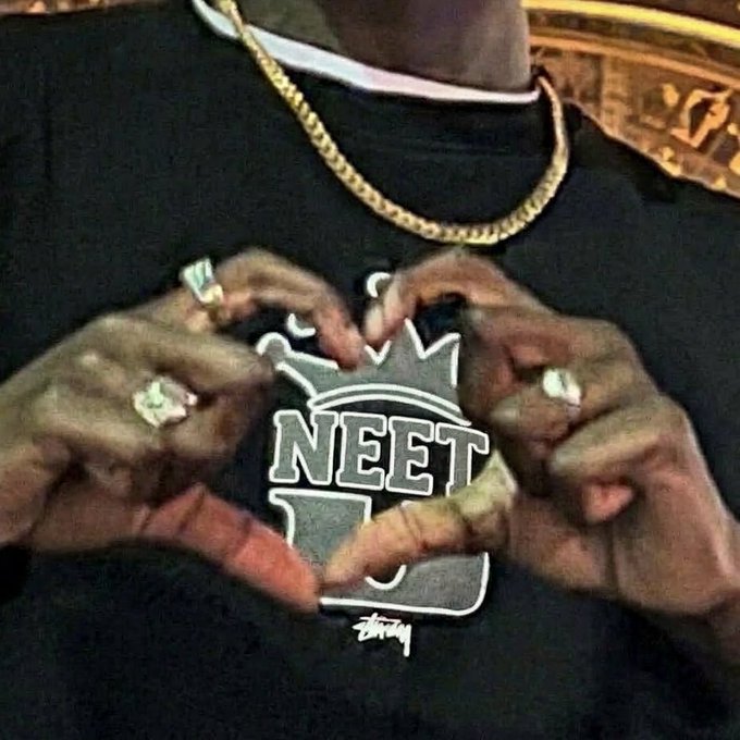 A man wearing a gold chain and diamond rings forms a heart shape with his hands over a black t-shirt featuring a "NEET" Stüssy logo graphic. The image visually reinforces the post's message of affection toward the $NEET ticker, with his hand-heart symbolizing love for the asset he rotated his gambling profits into.