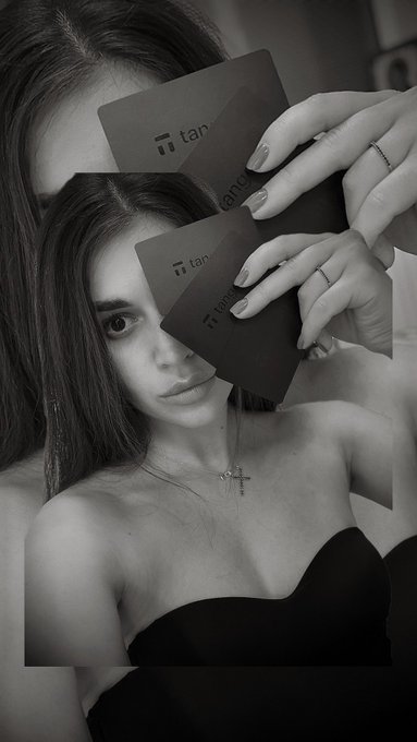 A black-and-white portrait shows a young woman holding two dark cards labeled "Tangem" in front of her face, styled like a mirror selfie. The image visually highlights the sleek, credit-card-sized Tangem cold wallets referenced in the post, emphasizing their portable, everyday form factor for secure crypto storage.