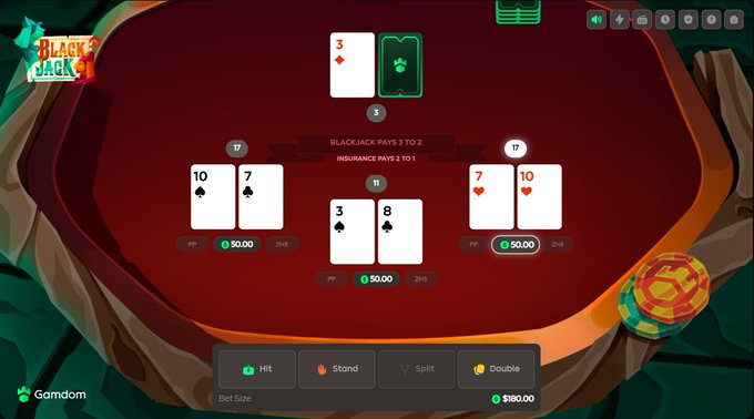 A digital blackjack table on Gamdom displays three active hands betting $50 each, with the player holding an 8 and 3 against a dealer's 3 (with a face-down card), and split hands showing 10/7 and 7/10. The interface offers Hit, Stand, Split, or Double options below, with $180.00 remaining in the bankroll, prompting players to share their move decision and Gamdom IDs.