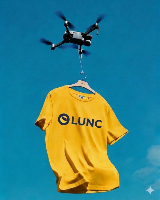 A drone hovers in a blue sky carrying a yellow t-shirt with the 'LUNC' logo (Terra Luna Classic cryptocurrency branding) hanging on a wooden hanger.