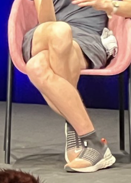 A seated person's muscular legs are crossed and bent in a way that resembles the Ethereum logo's diamond shape, as noted in the accompanying post highlighting the surprising resemblance. The person is wearing gray shorts and striped sneakers while sitting in a pink chair, with the unusual leg positioning creating an optical illusion of the cryptocurrency's symbol.