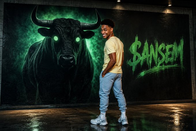 A young man poses in front of a large wall mural featuring a glowing-eyed black bull and the text "$ANSEM" in green graffiti-style lettering.