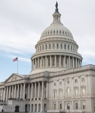 The image shows the U.S. Capitol Building in Washington, D.C., with an American flag waving in front of its iconic white dome and columns. The photo visually reinforces the post's subject matter by depicting the seat of U.S. legislative power, where the CLARITY Act is being negotiated and its revised text shared with key Senate Republicans.