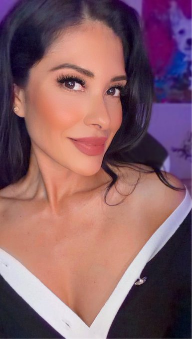 A woman with long dark hair, wearing a black and white off-the-shoulder top, poses for a close-up portrait with a soft smile and polished makeup. The image complements the post's confident self-promotion, visually reinforcing her message as a driven entrepreneur with a polished, professional image.