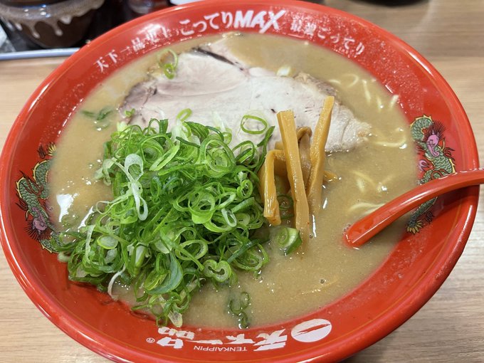 A bowl of Tenkaippin ("天下一品") Kotteri MAX ramen, featuring a rich, creamy tonkotsu-style broth topped with a generous mound of chopped green onions, chashu pork, and menma, served in the brand's signature red bowl with dragon designs. The post highlights a visit to the Tenkaippin Nonoichi Shinsho branch in Ishikawa Prefecture, praising the "kotteri MAX large" ramen with a large rice as their usual satisfying choice.
