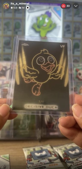 A hand holds up a black and gold "1/1 DECISIVE DUCK" trading card in a protective sleeve, matching the post's mention of pulling a 1/1 Neon Lights Decisive Duck Superfractor, with the username "its_a_mineral" visible at the top of the image.