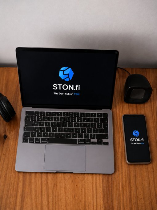 A silver laptop on a wooden desk displaying the STON.fi logo with the tagline 'The DeFi hub on TON' on its screen, alongside a smartphone showing the same logo and a small black speaker.