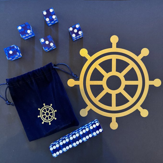 Blue translucent dice, dominoes, a velvet drawstring bag, and a yellow ship's wheel logo are arranged on a dark surface, suggesting a nautical or gaming theme.