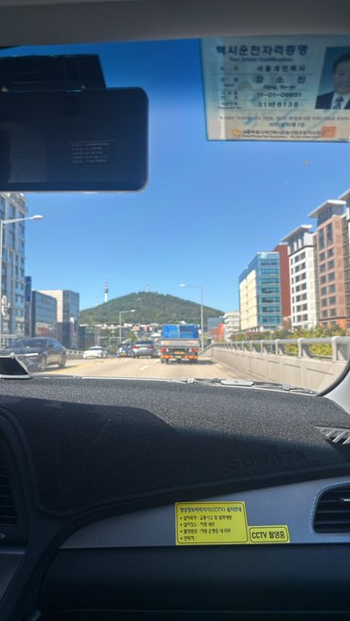 A view from inside a vehicle driving on a highway in South Korea, showing a toll pass receipt on the windshield, a dashcam, and a 'CCTV 녹화중' (CCTV recording) sticker on the dashboard.