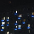 A dark nighttime photo showing a building with scattered illuminated windows, mostly with a blue/white glow.