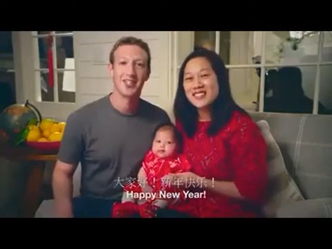 Mark Zuckerberg and Priscilla Chan pose with their baby daughter in red clothing, with text overlay reading '大家新年好！新年快乐！Happy New Year!'.