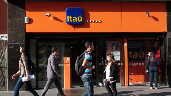 Pedestrians walk past an Itaú bank branch with its recognizable orange and blue signage, relating to the post about Brazil's largest bank Itaú testing tokenized bonds and investment funds on the blockchain.