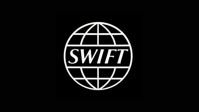 The image features a logo for SWIFT, which stands out against a black background. The logo consists of a white circle containing the word "SWIFT" written in capital letters inside. Below the logo, there's text that reads "JUST IN: SWIFT says a major ISO 20022 deadline is approaching. Starting in November 2026, non-compliant cross-border payment messages risk being rejected or delayed." This information suggests that the image might be related to an article discussing the impact of the ISO 20022 standard on SWIFT's operations and the importance of compliance with the new regulation.
