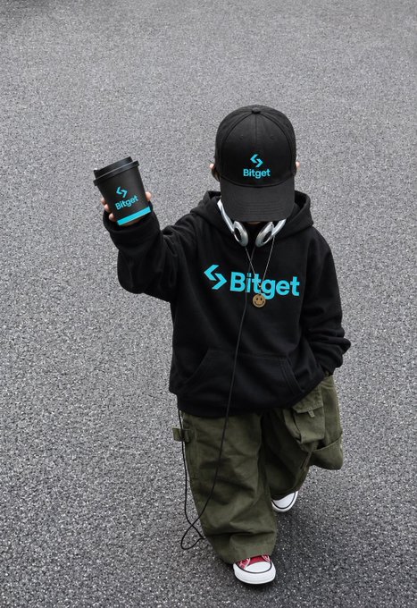 A child wearing a black hoodie, cap, and headphones branded with the 'Bitget' cryptocurrency exchange logo, holding a matching coffee cup.