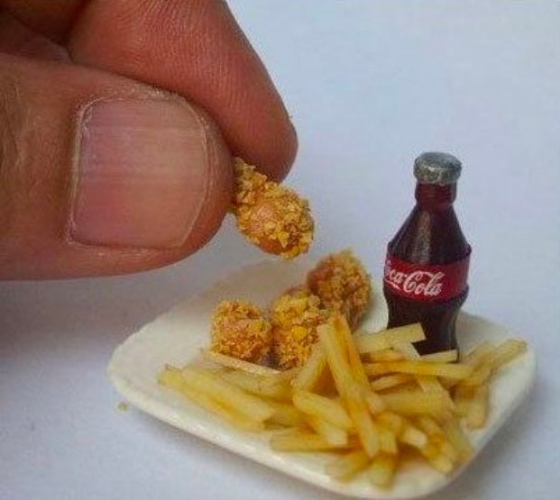 The image shows a miniature plate with two pieces of fried chicken, likely from a toy set or dollhouse, placed next to a Coca Cola bottle. The tiny size of both the food items and the bottle suggests that this meal could be part of a child's playtime or a creative display for an event like a fair or carnival.