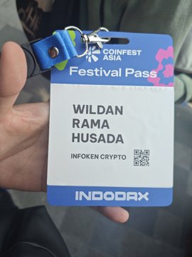 A hand holding a CoinFest Asia Festival Pass for WILDAN RAMA HUSADA with the tagline 'INFOKEN CRYPTO' and an INDODAX logo at the bottom.