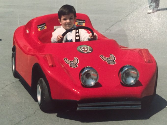 A young boy smiles while sitting behind the wheel of a red toy Lamborghini sports car, with vintage "Lamborghini" badges visible on the vehicle. The image plays on the phrase "og wen lambo guy" by showing a child as an original (OG) Lamborghini enthusiast, long before age made him a man.