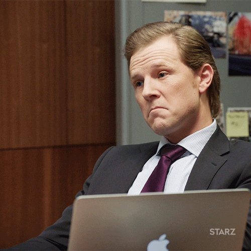 The image shows a man sitting at his desk with an Apple laptop computer open before him, looking down at something or someone off-camera. There are several notes attached to the wall behind him, which could be related to the content of the show he is watching on Starz. The focus of the post seems to be on the character's facial expression and body language, suggesting that it might be a scene from a TV show or movie featuring this character.