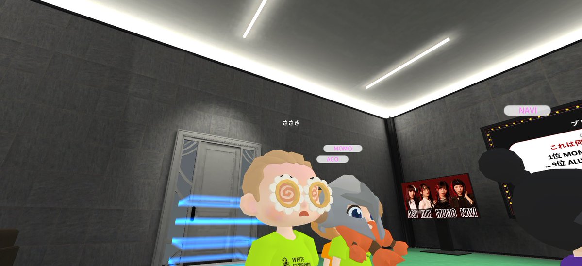 A screenshot from a virtual reality or game environment showing avatar characters labeled 'MOMO', 'ACO', and 'NAVI' standing in a room with a poster of four women.