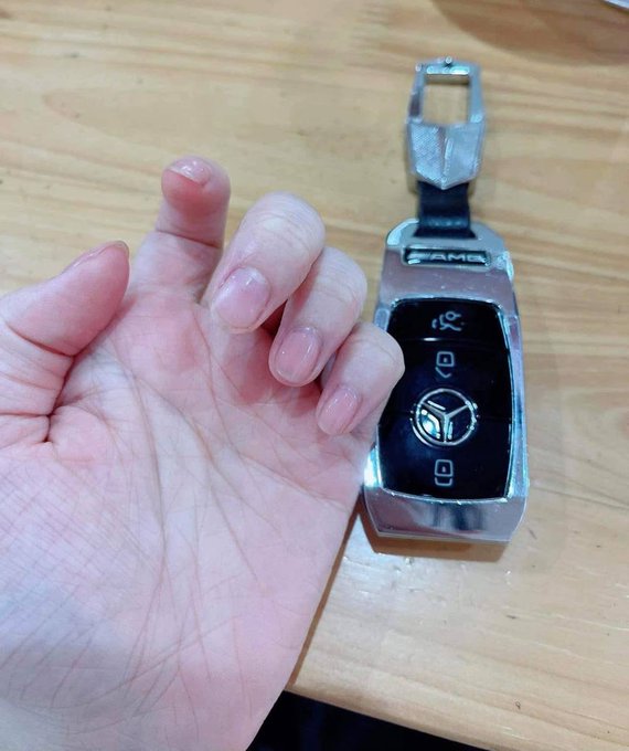 A hand with short, unpainted nails is held up next to a Mercedes-Benz car key fob (with "AMG" visible) on a wooden surface, humorously illustrating the joke about having "two white hands" as one's only assets while watching others make money online.