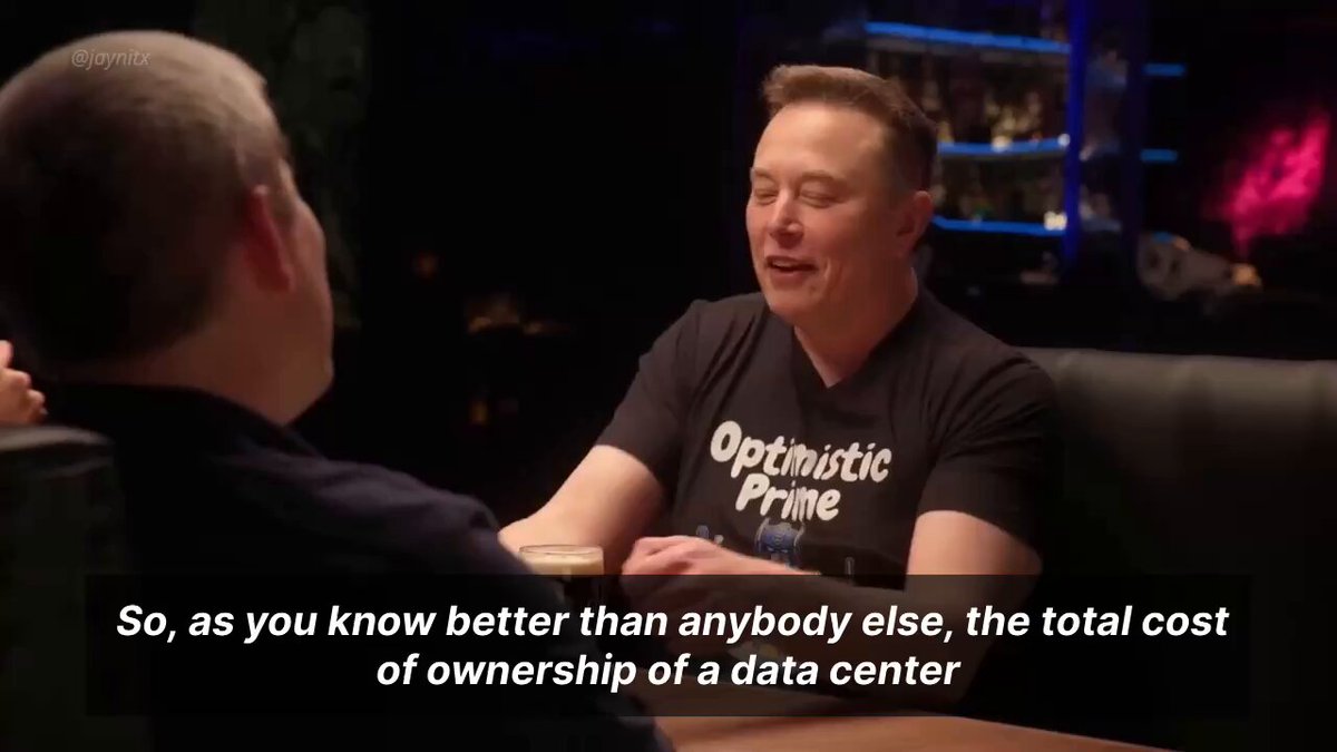 ersin, a renowned tech expert and founder of SpaceX, sits across from another individual at a table with a laptop open on the surface.