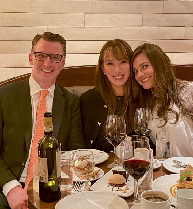 Three well-dressed diners smile at the camera while enjoying wine and desserts at an upscale restaurant, their elegant table setting and celebratory mood capturing the social spirit of a Bitcoin Mondays gathering in Manhattan.