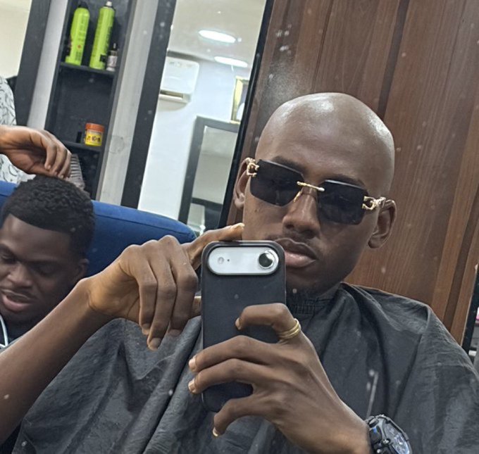 A man wearing designer sunglasses takes a mirror selfie with his phone, displaying a confident expression with a subtle smirk. The accompanying post celebrates a successful trade where $70 was turned into $1,500 on $SUNUSI, capturing the smug satisfaction of a profitable crypto win.