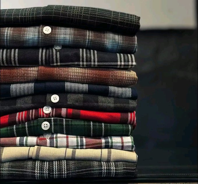 A neatly stacked pile of folded plaid and checkered flannel shirts in various colors including red, green, blue, brown, and black, with visible buttons.